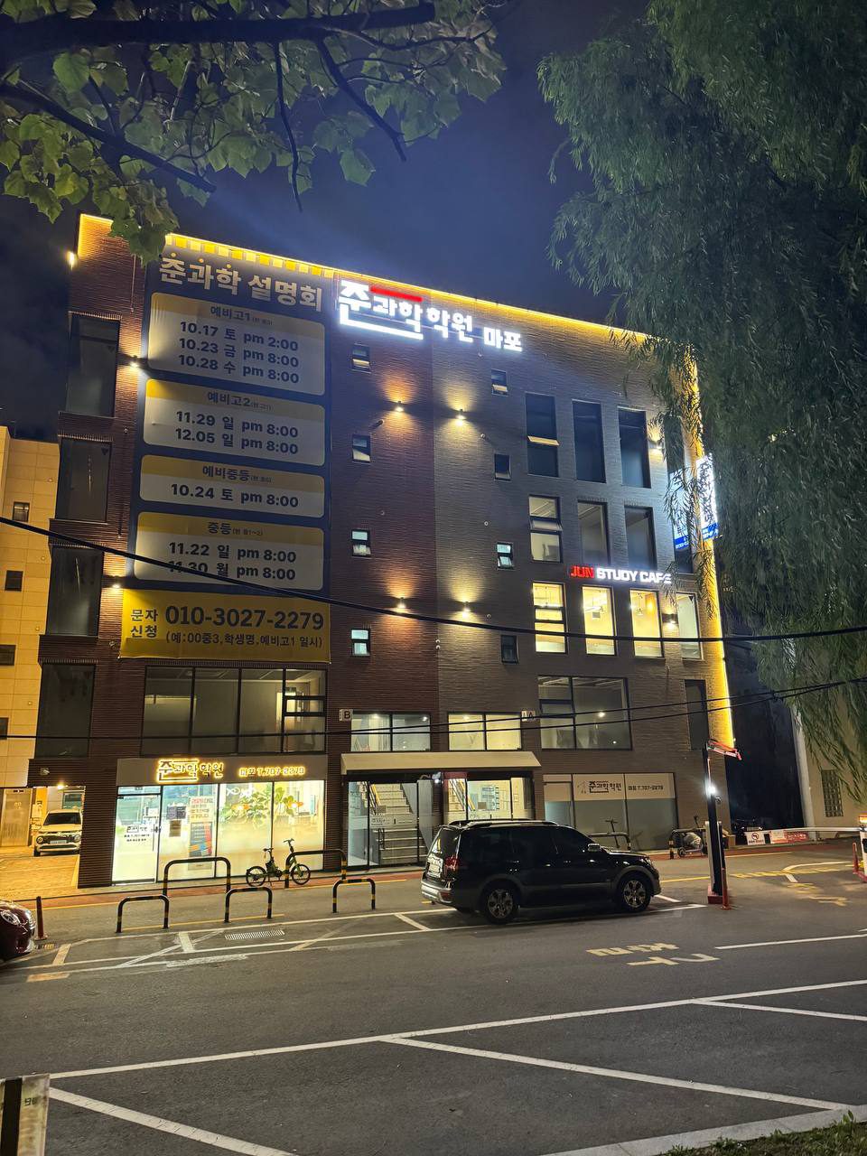 준과학학원 마포 간판과 커다란 설명회 현수막이 걸린 건물 앞에 검은 차량이 서 있고, 위로 나뭇가지가 드리워져 있다