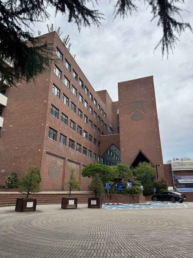삼각형 모양의 입구와 유리창이 있는 붉은 벽돌 다산관, 앞쪽에는 나무와 포장된 광장이 보인다