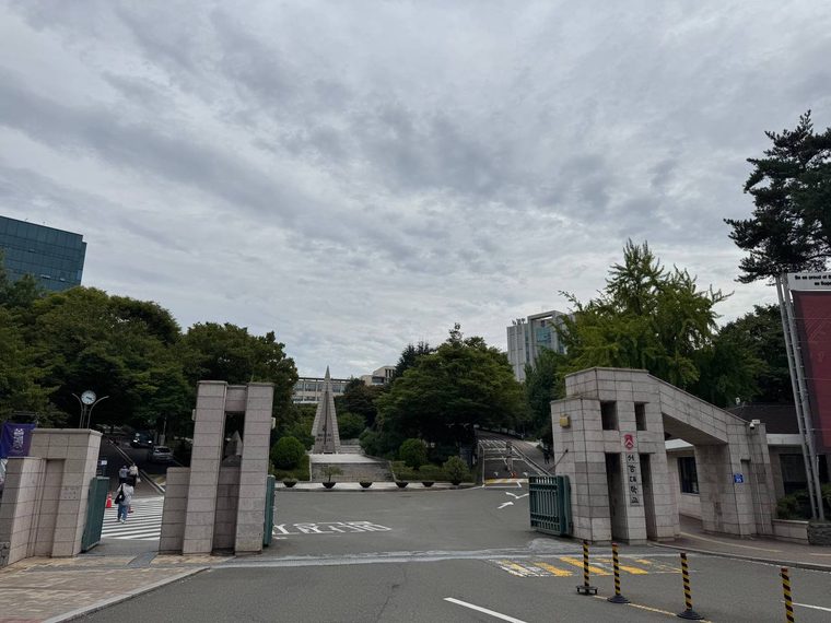 화강암 기둥 사이로 보이는 서강대 정문 안쪽, 가운데 오벨리스크 모양 알바트로스탑과 계단, 양옆으로 우거진 나무