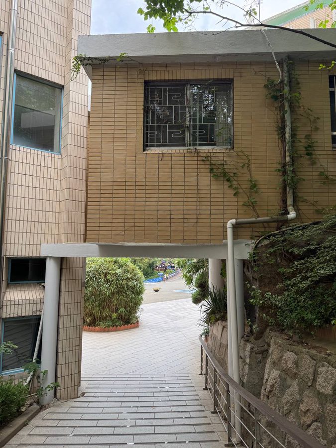 베이지색 타일 건물 아래로 열린 통로와 내려가는 계단, 오른쪽 바위와 난간이 보이는 서강대 폭풍의 언덕